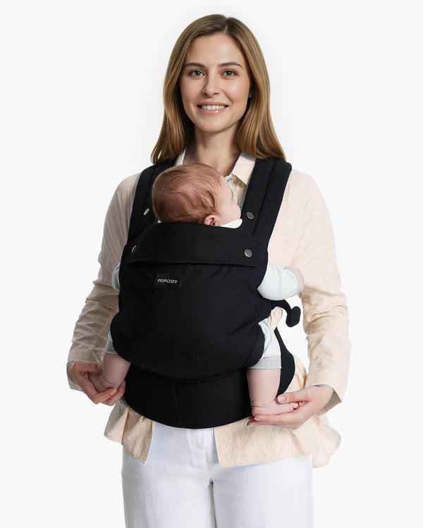 Momcozy PureHug Baby Carrier. Black carrier, comfortable design, worn by mother holding baby. Ideal for babywearing.