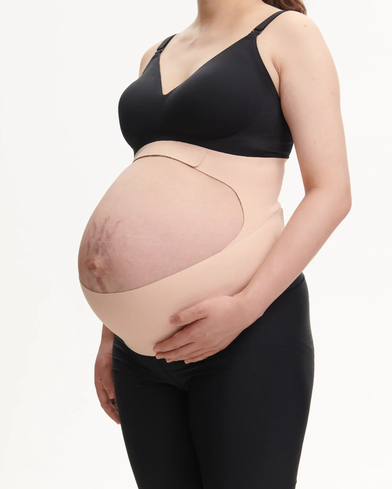 Translation missing: en.Pregnant person modeling a beige BumpEase Momcozy Ergonest maternity belly band over black leggings and nursing bra